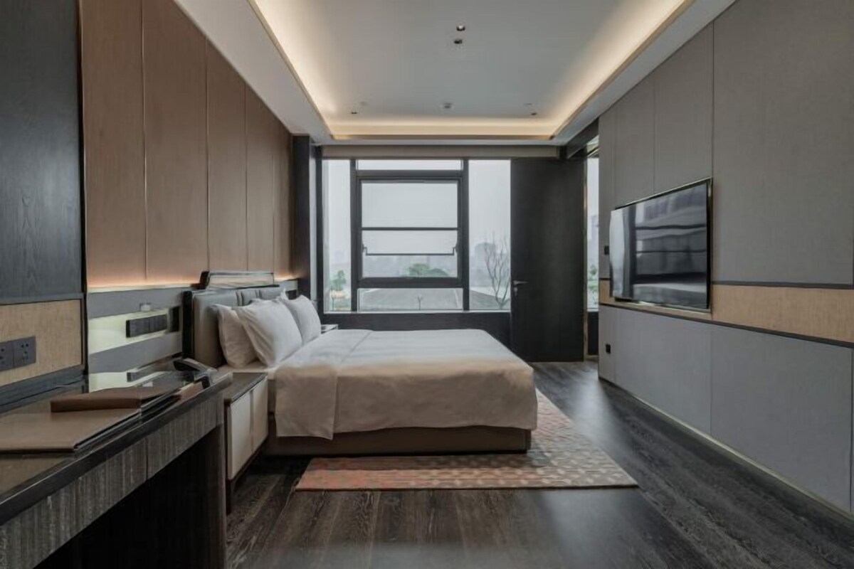 A modern bedroom with a large bed, a desk, and a TV.