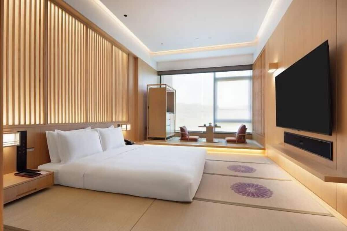 A modern hotel room with a large bed, a flat-screen TV, and a view of the city.