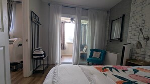 A bedroom with a bed, a blue armchair, a heater, a window with curtains, and a view to the outside. - Downtown/Midtown "Family ATL CityScape" (Atlanta)