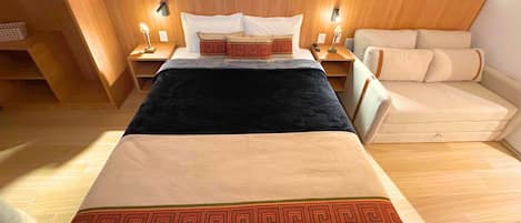 A hotel room with a bed, bedside tables, a sofa, and a wooden floor.