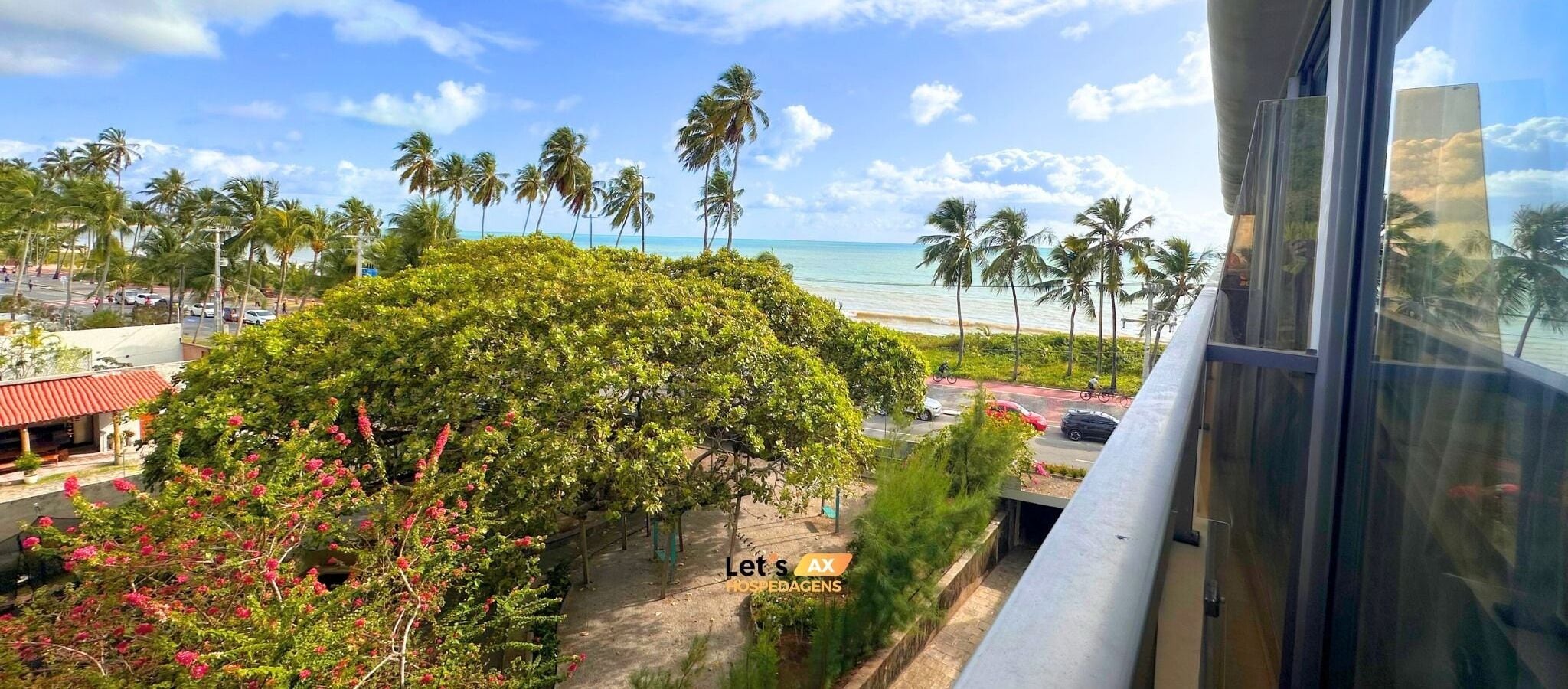 Vista dalla finestra su una spiaggia con palme e un edificio con tetto rosso.