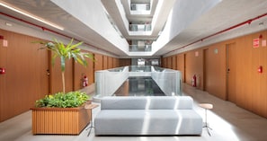 A modern hotel lobby with a central staircase, wooden paneling, and a seating area.
