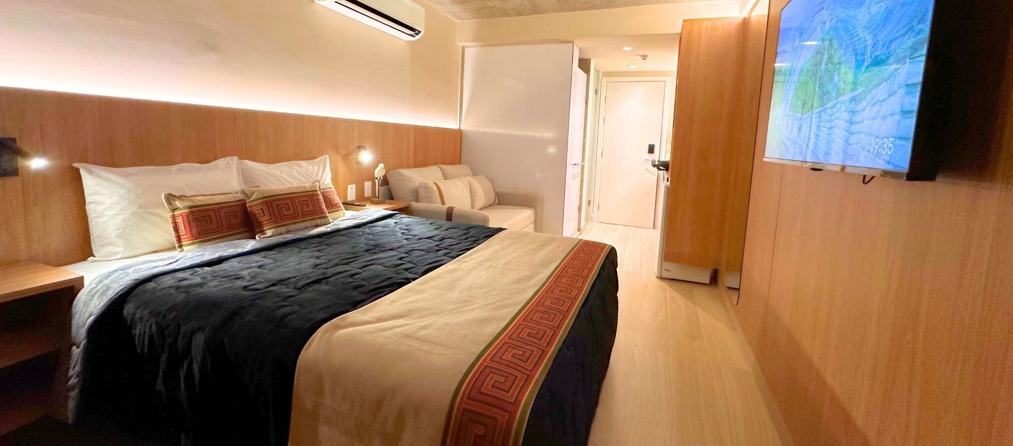 Ein Hotelzimmer mit einem Bett, Nachttischen, einem Fernseher und einer Tür zu einem weiteren Raum.