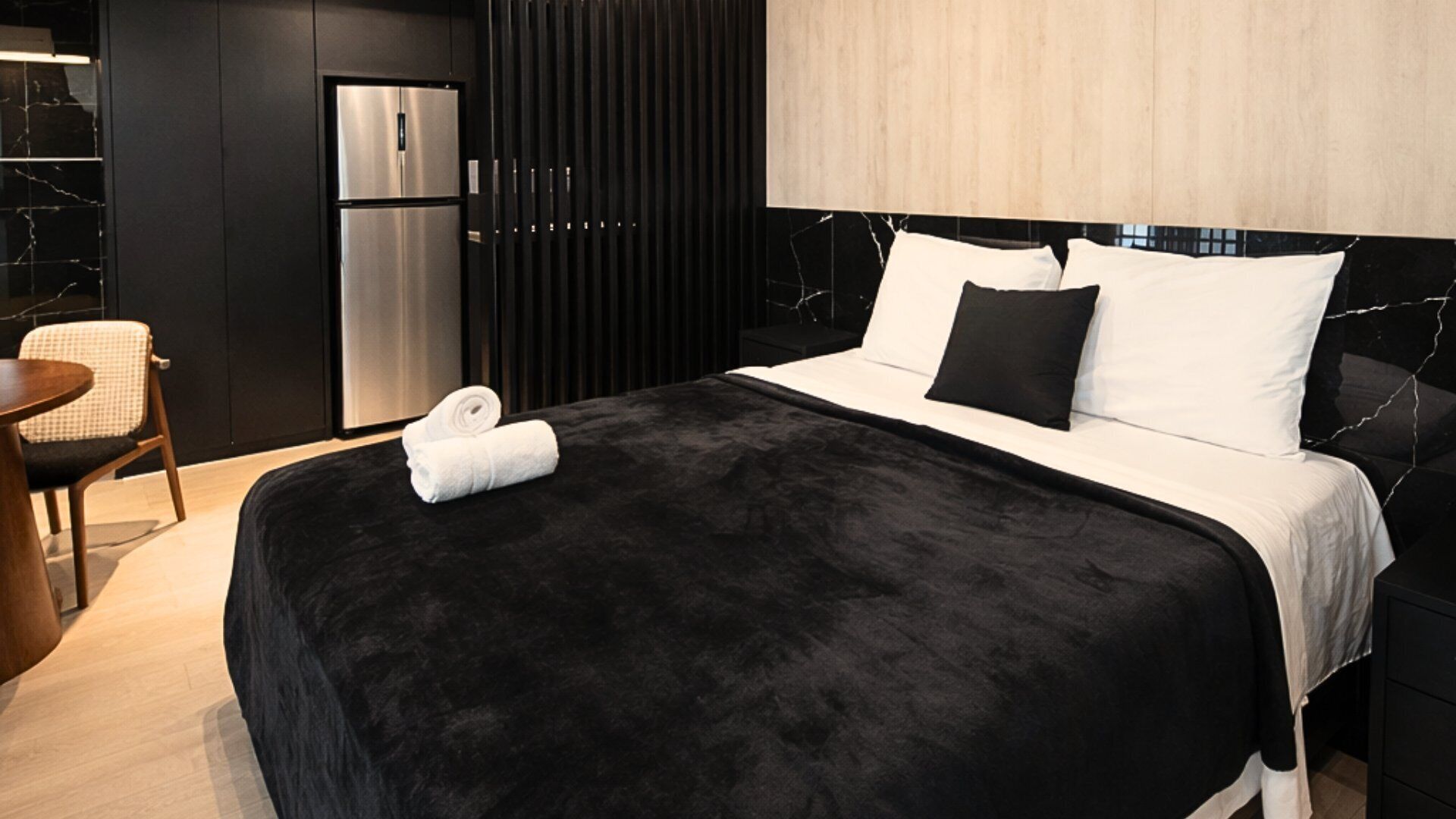 Een moderne hotelkamer met een groot bed, kleurenschema in zwart en wit, een ingebouwde koelkast en een houten hoofdeinde.