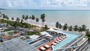 A rooftop pool area with lounge chairs and umbrellas, overlooking a beach with palm trees and a clear sky. - AX Setai Yacht (João Pessoa)