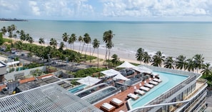 A rooftop pool area with lounge chairs and umbrellas, overlooking a beach with palm trees and a clear sky. - AX Setai Yacht (João Pessoa)