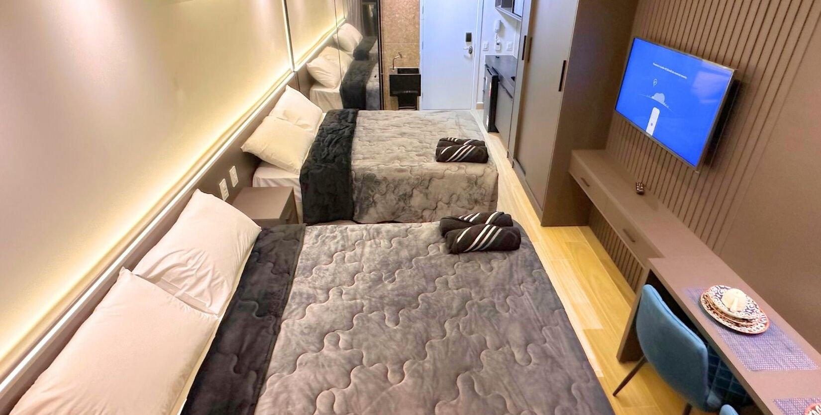 A hotel room with two beds, a TV, a desk, and a chair.