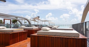 A deck with wooden benches and cushions, a glass railing, and a view of the sea. - AX Setai Yacht (João Pessoa)