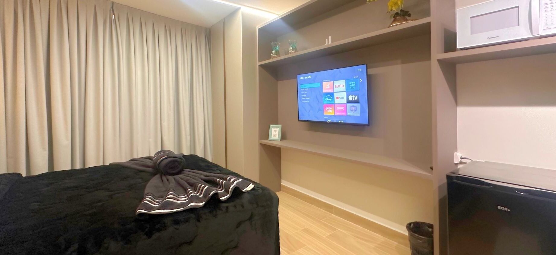 Una habitación con una cama, un televisor en la pared, un microondas y un pequeño cubo de basura.