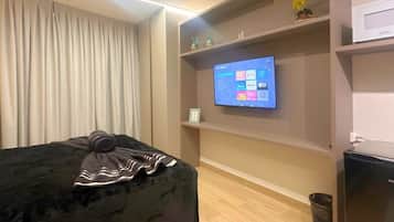 Ein Zimmer mit einem Bett, einem an der Wand montierten Fernseher, einer Mikrowelle und einem kleinen Mülleimer.