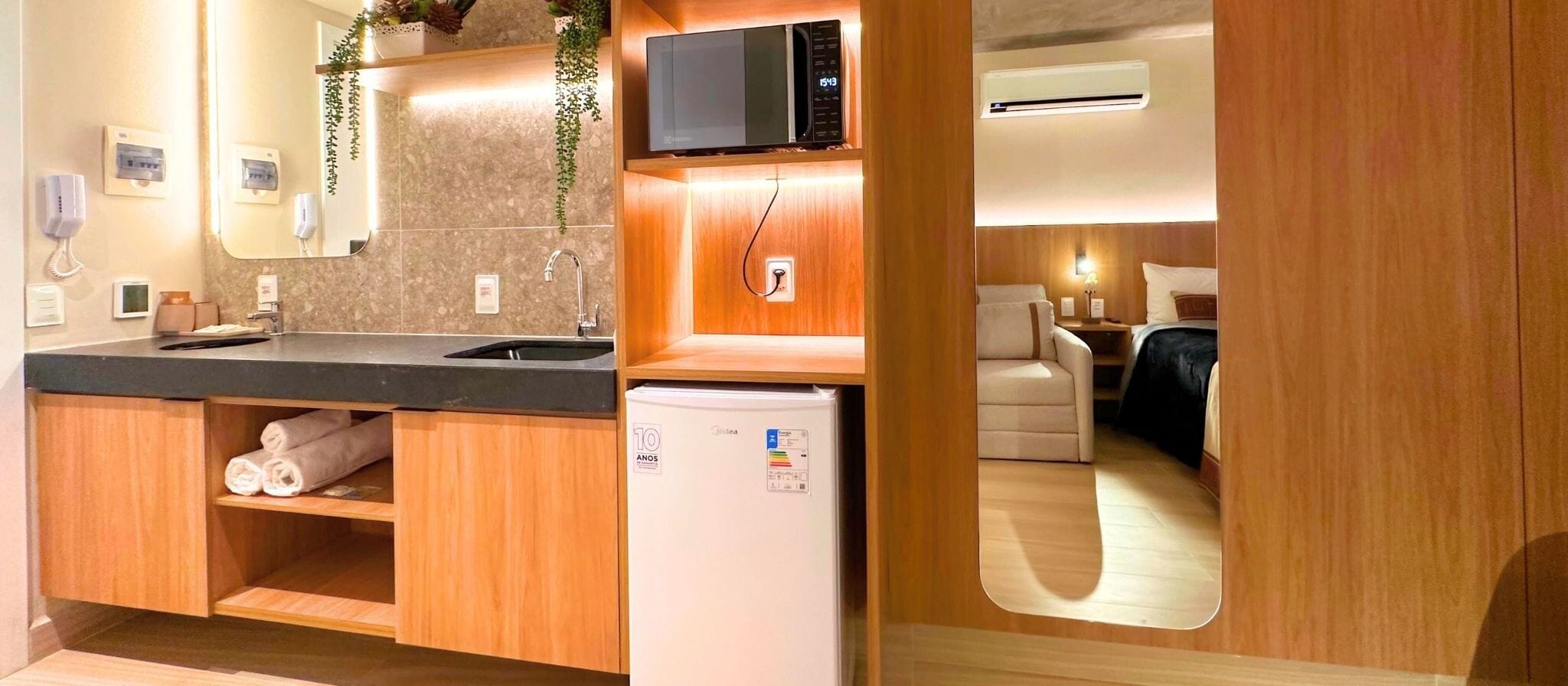 A compact kitchenette with a microwave, a small refrigerator, a sink, and a mirror.