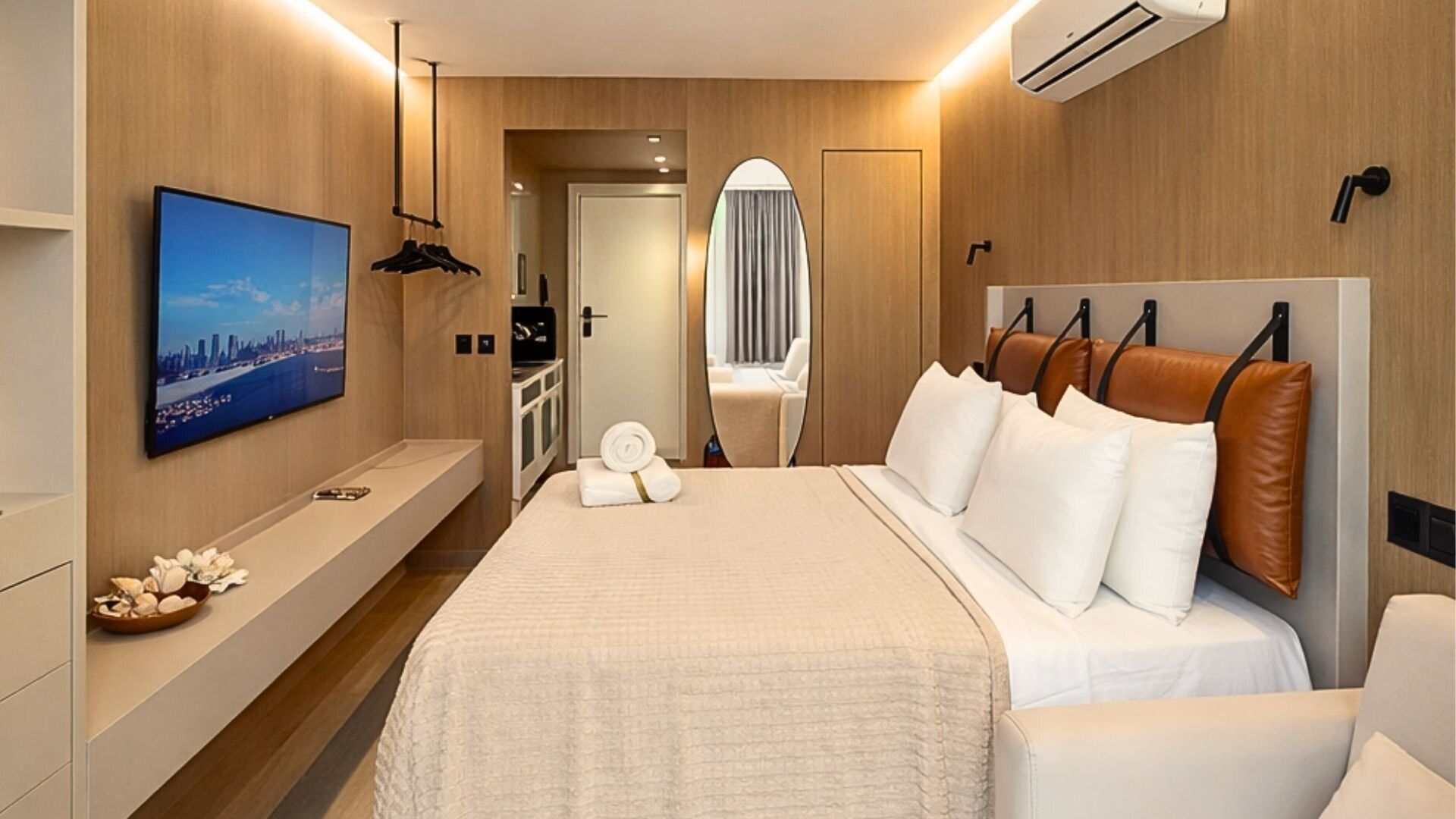 Quarto de hotel com cama, televisão, espelho, guarda-roupa e casa de banho visível através de uma porta aberta.