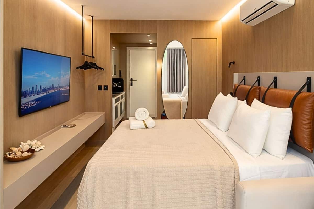 A hotel room with a bed, a TV, a mirror, a wardrobe, and a bathroom visible through an open door.
