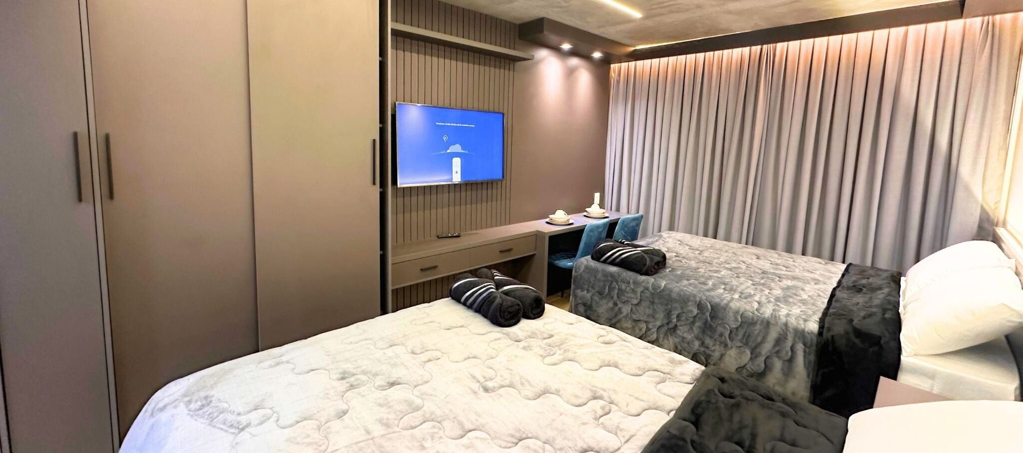 Een hotelkamer met twee bedden, een televisie, een bureau en een raam met gordijnen.