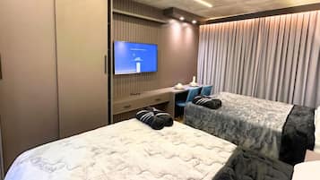 Quarto de hotel com duas camas, televisão, escrivaninha e janela com cortinas.