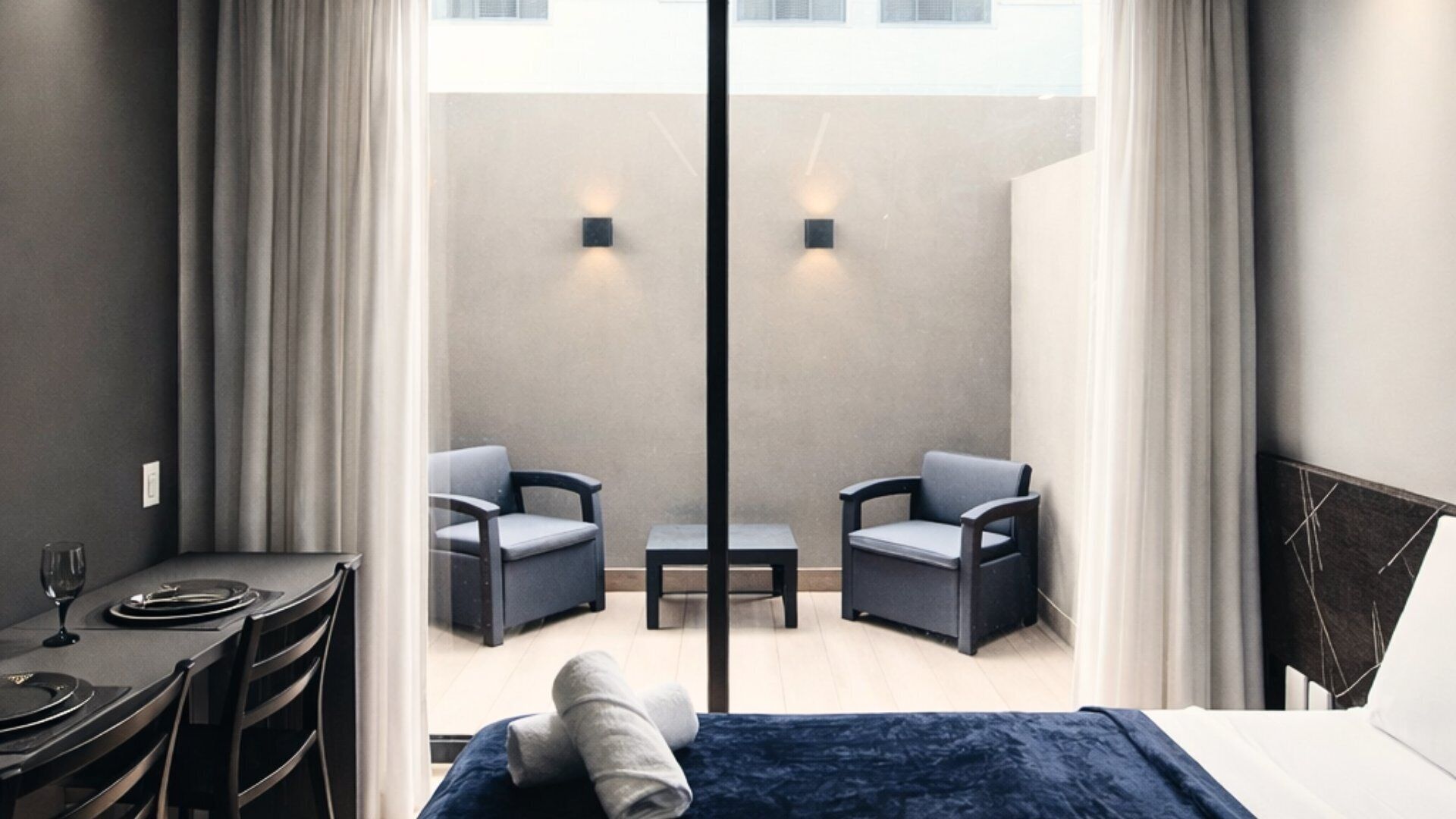 Et moderne hotelværelse med balkon, to stole, et lille bord og en seng.