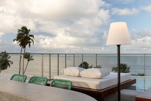 A balcony with a bed, green chairs, a lamp, and a view of the sea. - AX Setai Yacht (João Pessoa)
