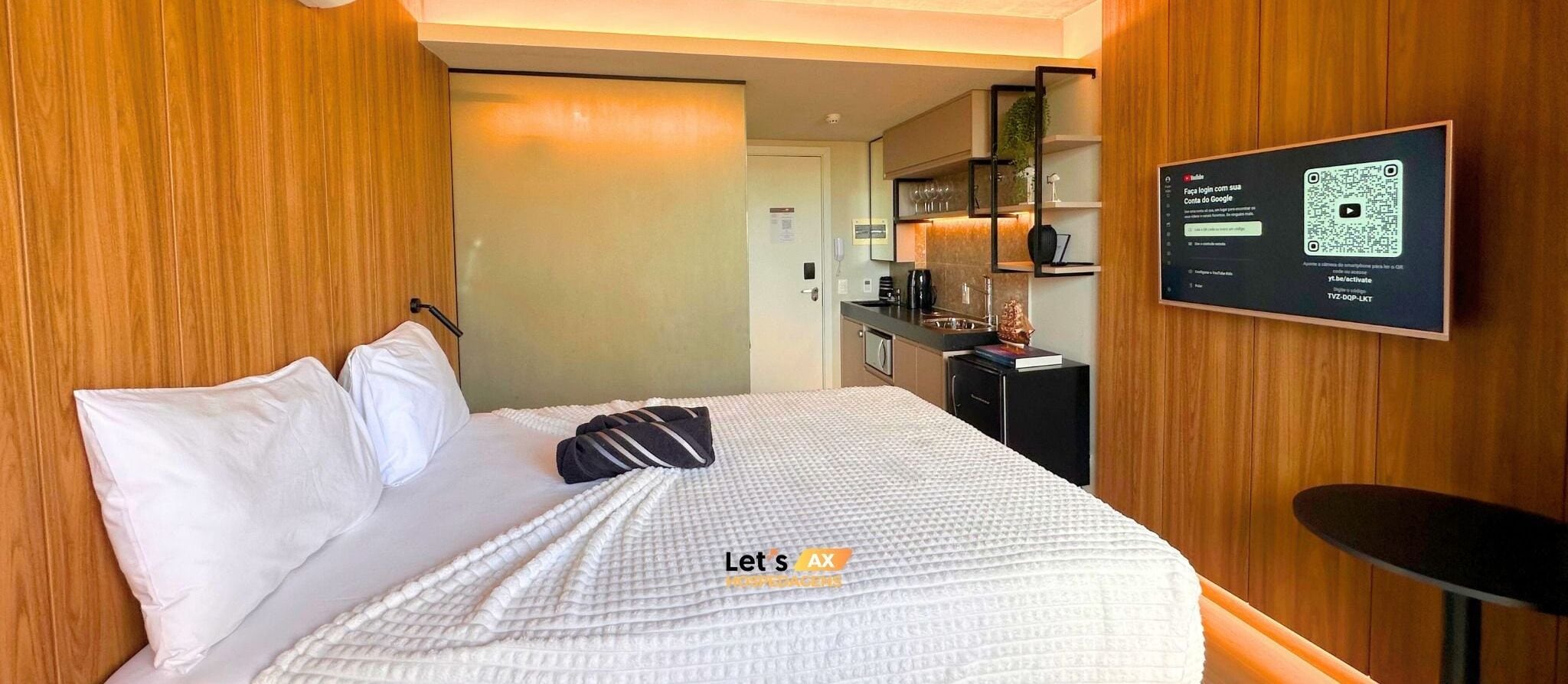 A hotel room with a bed, a desk, a chair, a TV screen, and a wooden wall.