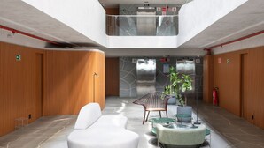 A modern lobby with a high ceiling, wooden panel walls, a central seating area with a white sofa and green chairs, and an elevator in the background. - AX Setai Yacht (João Pessoa)
