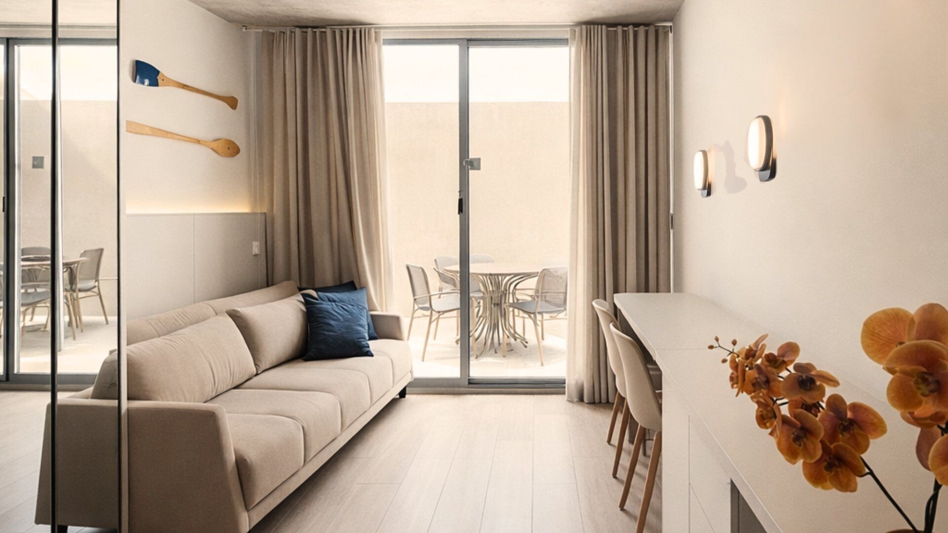 A modern living room with a sofa, dining table, chairs, and a sliding glass door leading to an outdoor area.