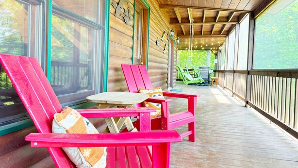 Eine hölzerne Veranda mit zwei roten Adirondack-Stühlen, einem kleinen Tisch und einer Hängematte.