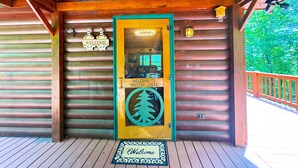 Ein Eingang zu einer Holzhütte mit einer grünen Tür, einer Fußmatte und einem Schild mit der Aufschrift 'Welcome to Treetop Lodge'.