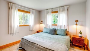A bedroom with a large bed, two bedside tables, a nightstand with a lamp, and a window with curtains. - Bay City Retreat ~ 1/2 Mi to Local Beach! (Bay City)