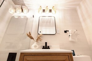 A modern bathroom with a white vanity, a mirror, and three wall-mounted lights. - Beach Front Beautiful New Apartment with Pool in Miami Beach. (Miami Beach)