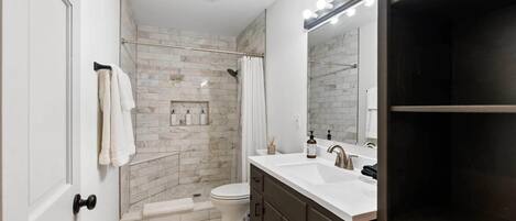 Un baño moderno con ducha, inodoro, tocador y un espejo grande con iluminación.