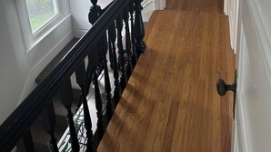A hallway with wooden flooring, white walls, and a black railing.