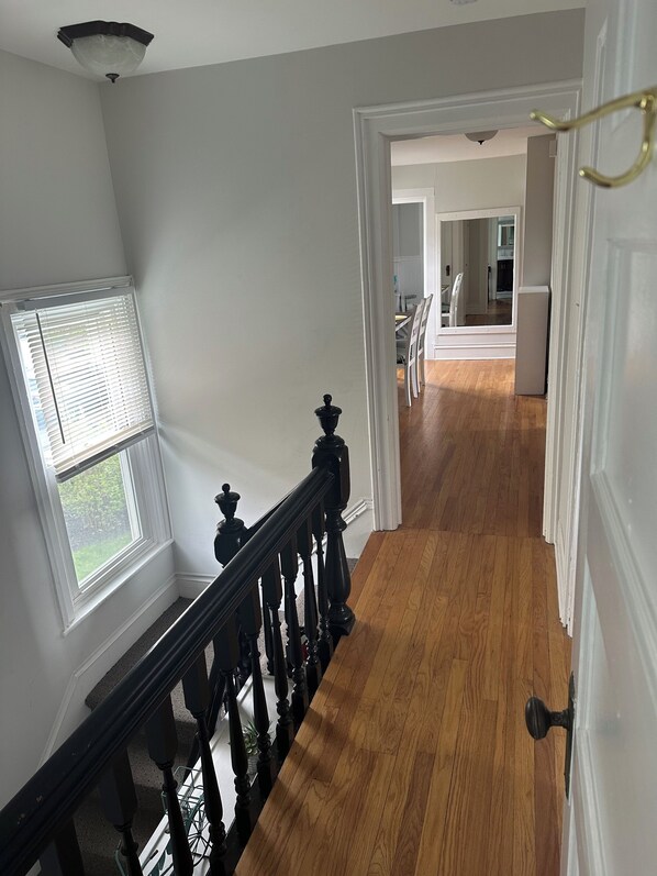 A hallway with wooden flooring, white walls, and a black railing.