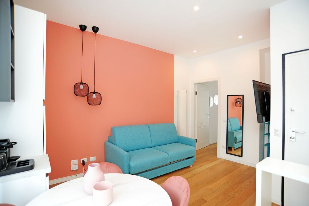 Ein modernes Wohnzimmer mit einem blauen Sofa, einem runden Tisch mit rosa Stühlen und einer Küchenzeile mit weißer Arbeitsplatte.