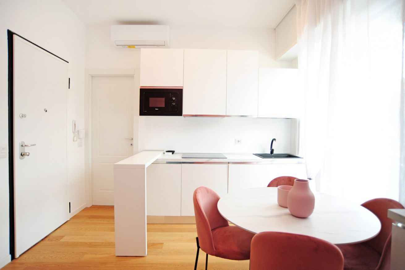 A modern kitchen with white cabinetry, a built-in microwave, and a dining area with a white table and red chairs.