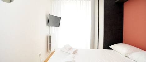 A hotel room with a bed, white towels, a TV, and a window with curtains.