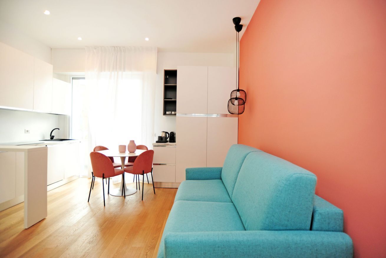 Una cucina moderna con mobili bianchi, un tavolo da pranzo con sedie rosse e un divano blu su una parete color pesca.