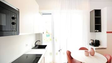 Una cucina moderna con un piano cottura nero, mobili bianchi e un'area pranzo con un tavolo rotondo e sedie rosse.