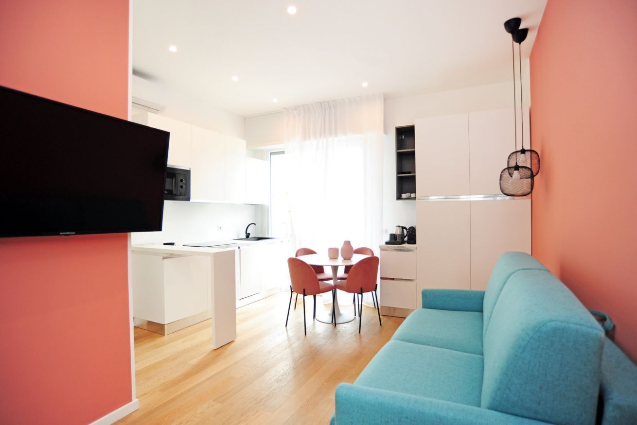 Un soggiorno moderno con un divano blu, un tavolo da pranzo con sedie, una zona cottura con forno a microonde e una TV a parete.