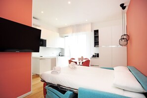 A modern hotel room with a bed, a desk, a chair, a television, and a kitchenette. - San Giusto Apartment (Milano)