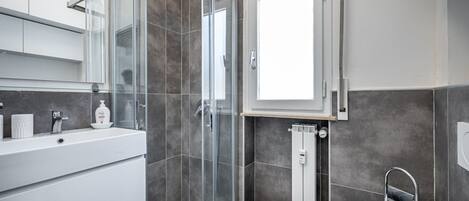 A modern bathroom with a glass-enclosed shower, a white vanity with a mirror, and a window providing natural light.