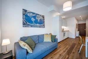 A modern living room with a blue sofa, a world map artwork, and a kitchen in the background.