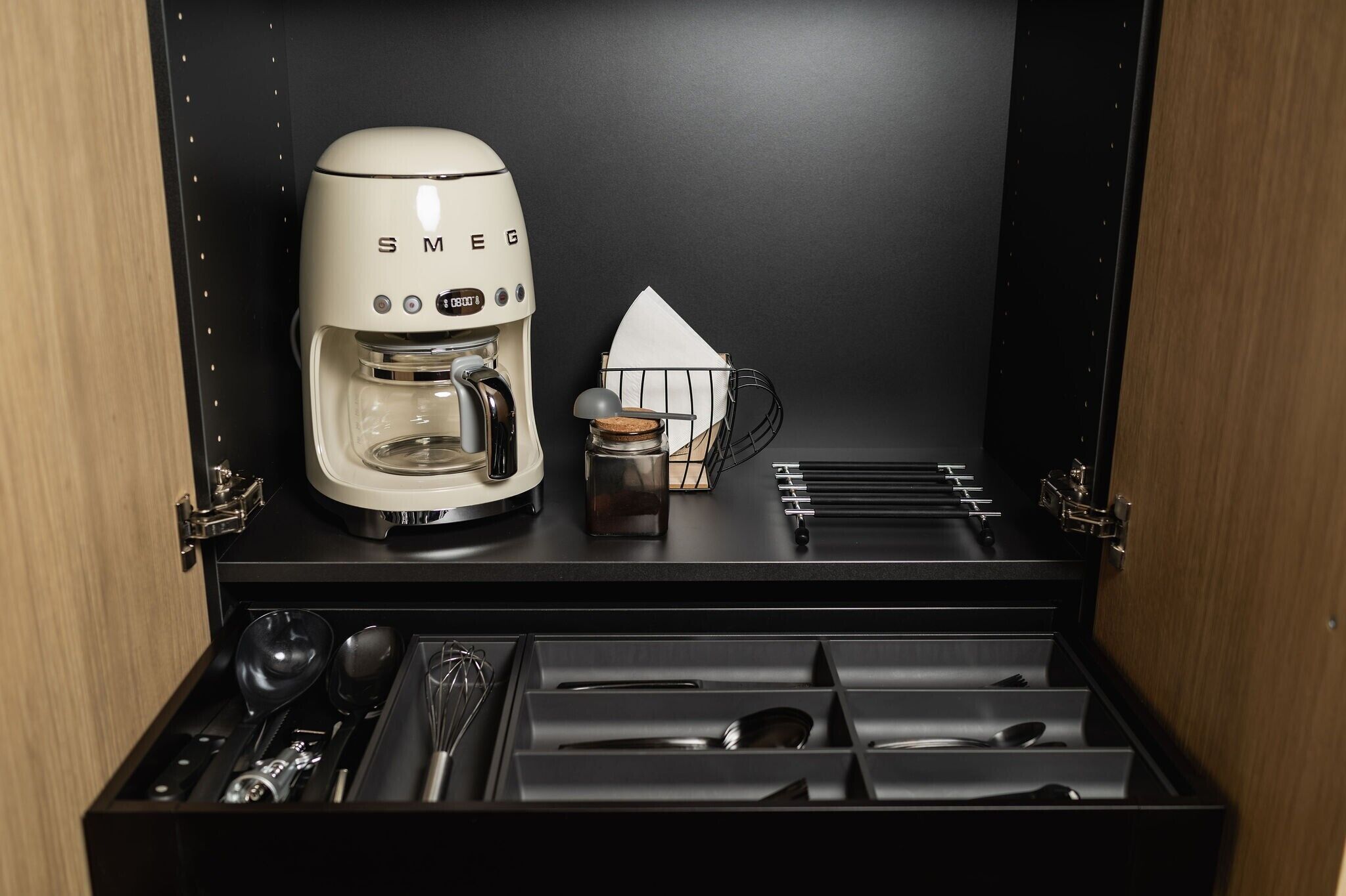 Une cuisine compacte avec une machine à café blanche, un petit bocal et un porte-ustensiles.