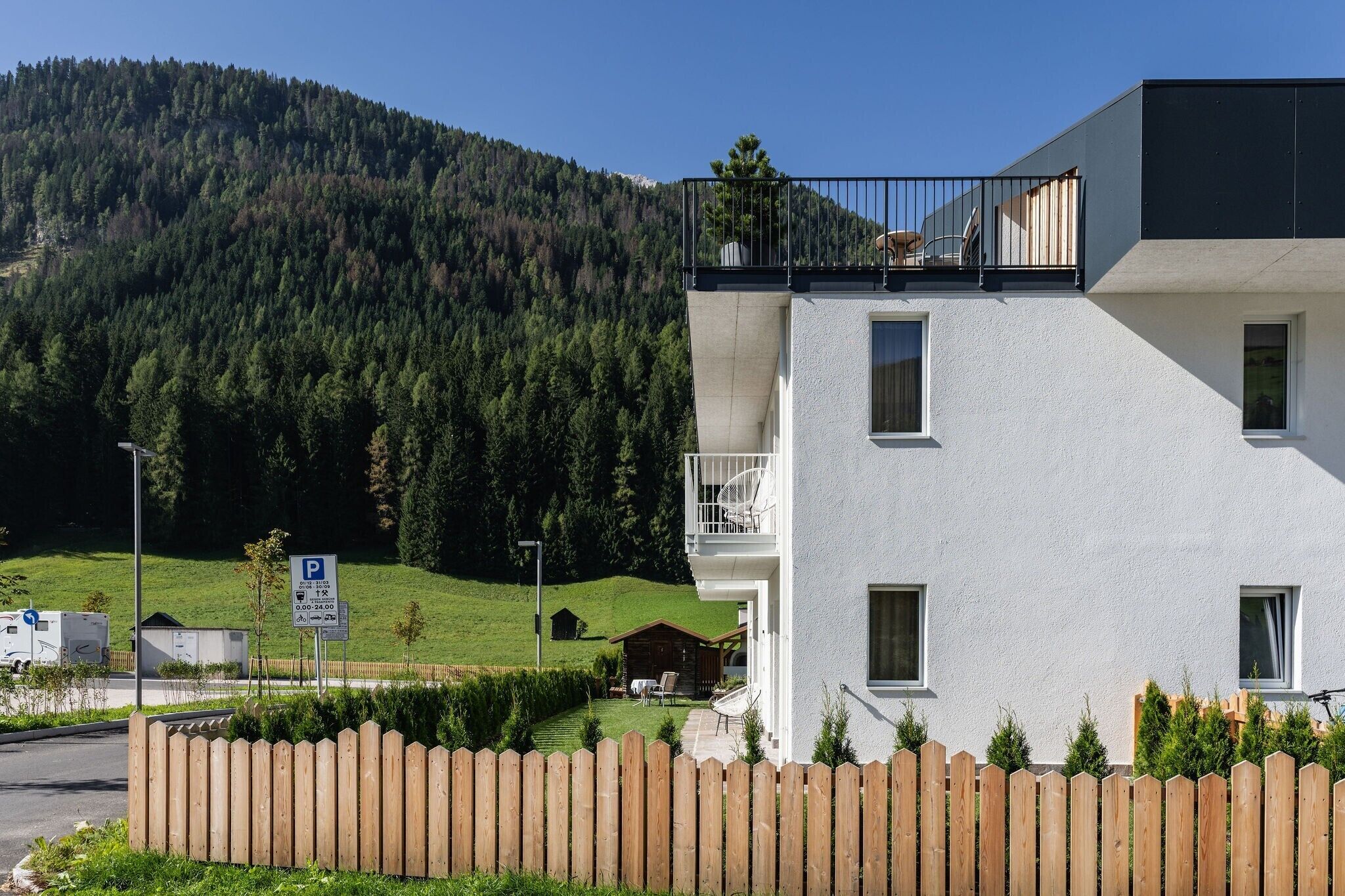 A modern building with a balcony, a parking sign, and a mountainous backdrop.