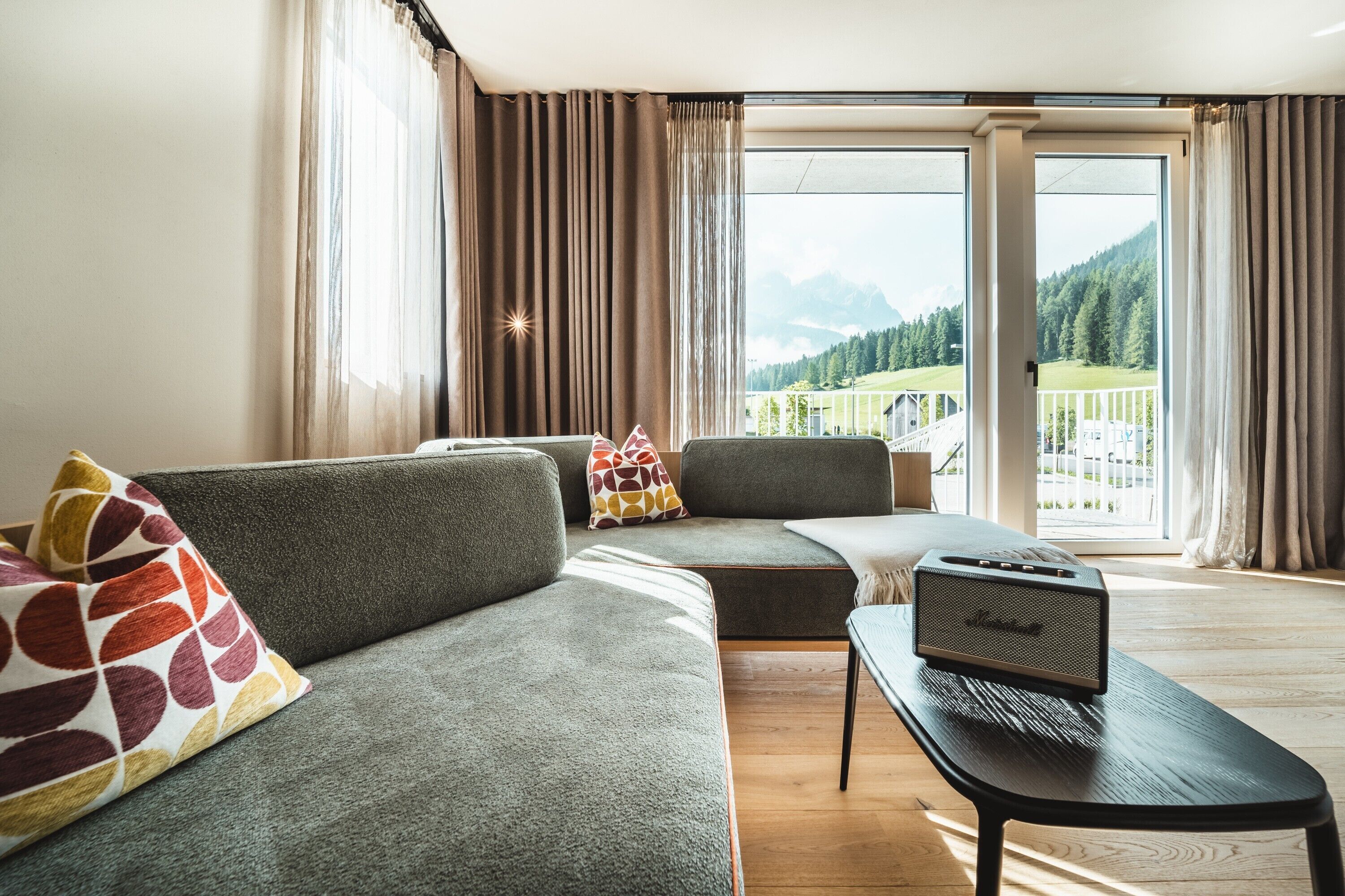 Una sala de estar moderna con un sofá, una mesa de centro y vistas a un balcón con paisaje de montaña.