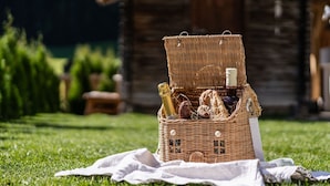 Una cesta de mimbre para picnic sobre césped, con un paño, cerca de una construcción de madera.