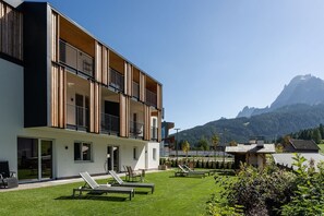 Un bâtiment moderne doté de balcons, d’une pelouse verdoyante et offrant une vue sur la montagne.