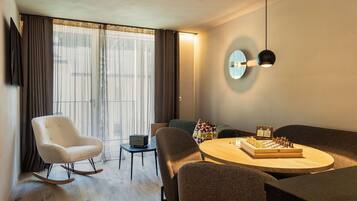 Un salon moderne avec une table ronde en bois, un fauteuil à bascule blanc, un canapé et un téléviseur fixé au mur.