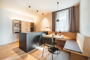Une cuisine compacte dotée d’un îlot central intégré, d’un coin repas avec un banc et d’une fenêtre agrémentée de rideaux.
