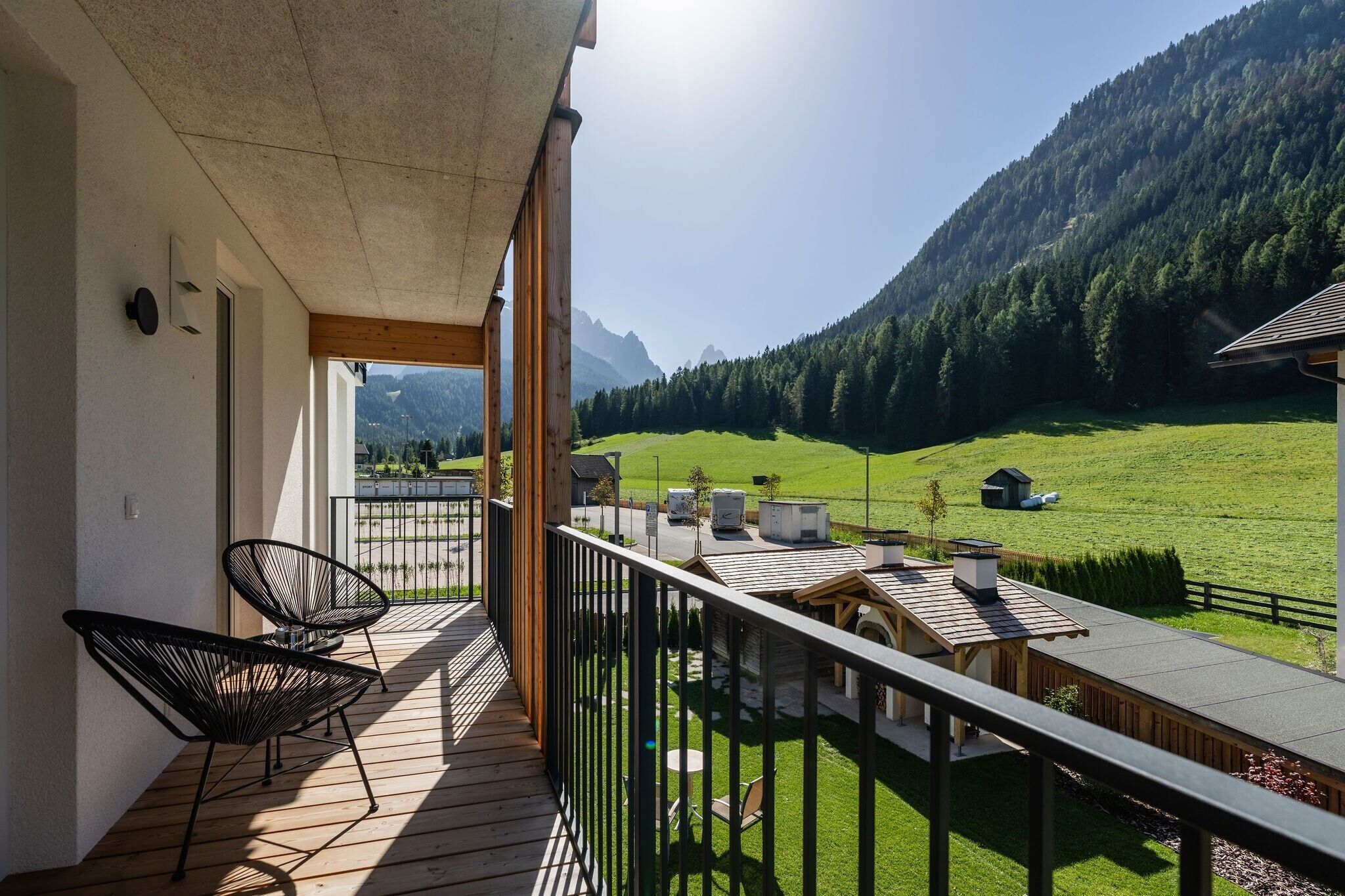 Un balcone con sedie, vista su un prato verde e montagne sullo sfondo.