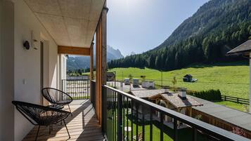 Un balcone con sedie, vista su un prato verde e montagne sullo sfondo.