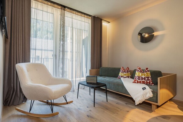 Un salon moderne avec un fauteuil à bascule, un canapé agrémenté de coussins à motifs, un ordinateur portable posé sur une petite table et un luminaire fixé au mur.